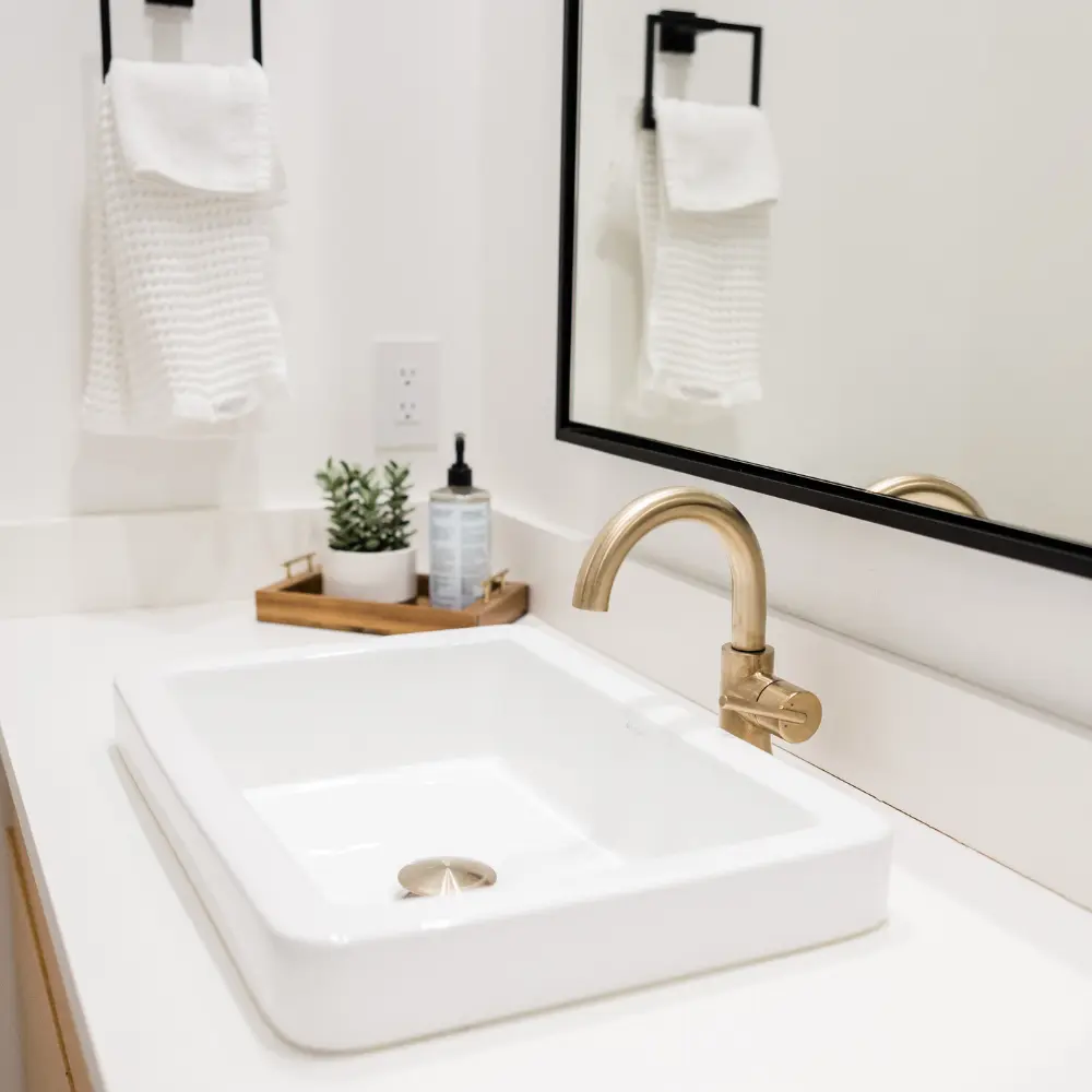 Lavabo design avec un robinet doré, miroir encadré et décoration minimaliste dans une salle de bain moderne plomberie à Mâcon